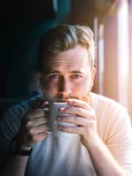 Man in sweater drinking from white mug with steam rising