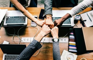 Four people doing a team fist bump over a desk with laptops