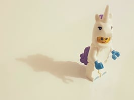 LEGO minifigure in white unicorn costume with purple mane and blue accessories