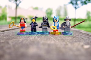 Five LEGO minifigures including Wonder Woman, Batman, and Sonic standing on circular bases
