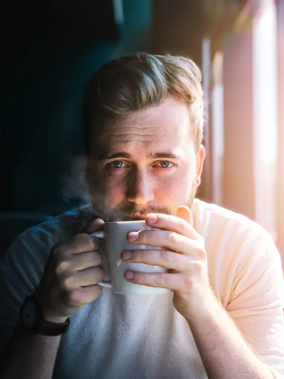 Man in sweater drinking from white mug with steam rising