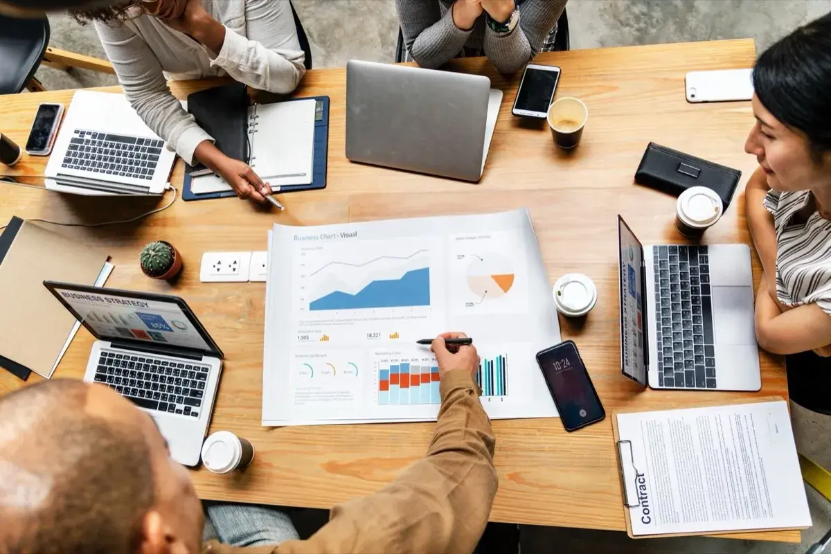 Business team analyzing charts and data around conference table with laptops