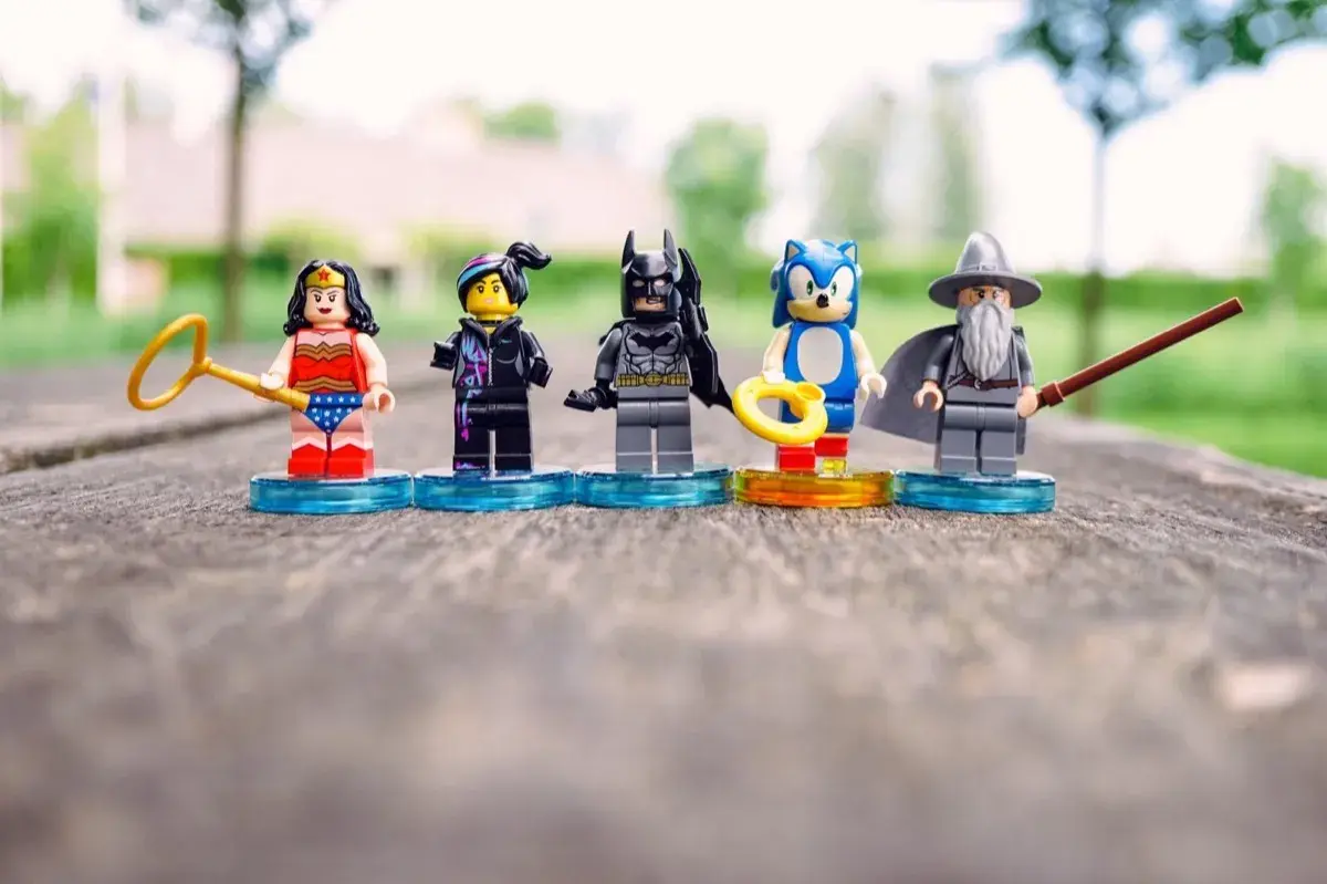 Five LEGO minifigures including Wonder Woman, Batman, and Sonic standing on circular bases