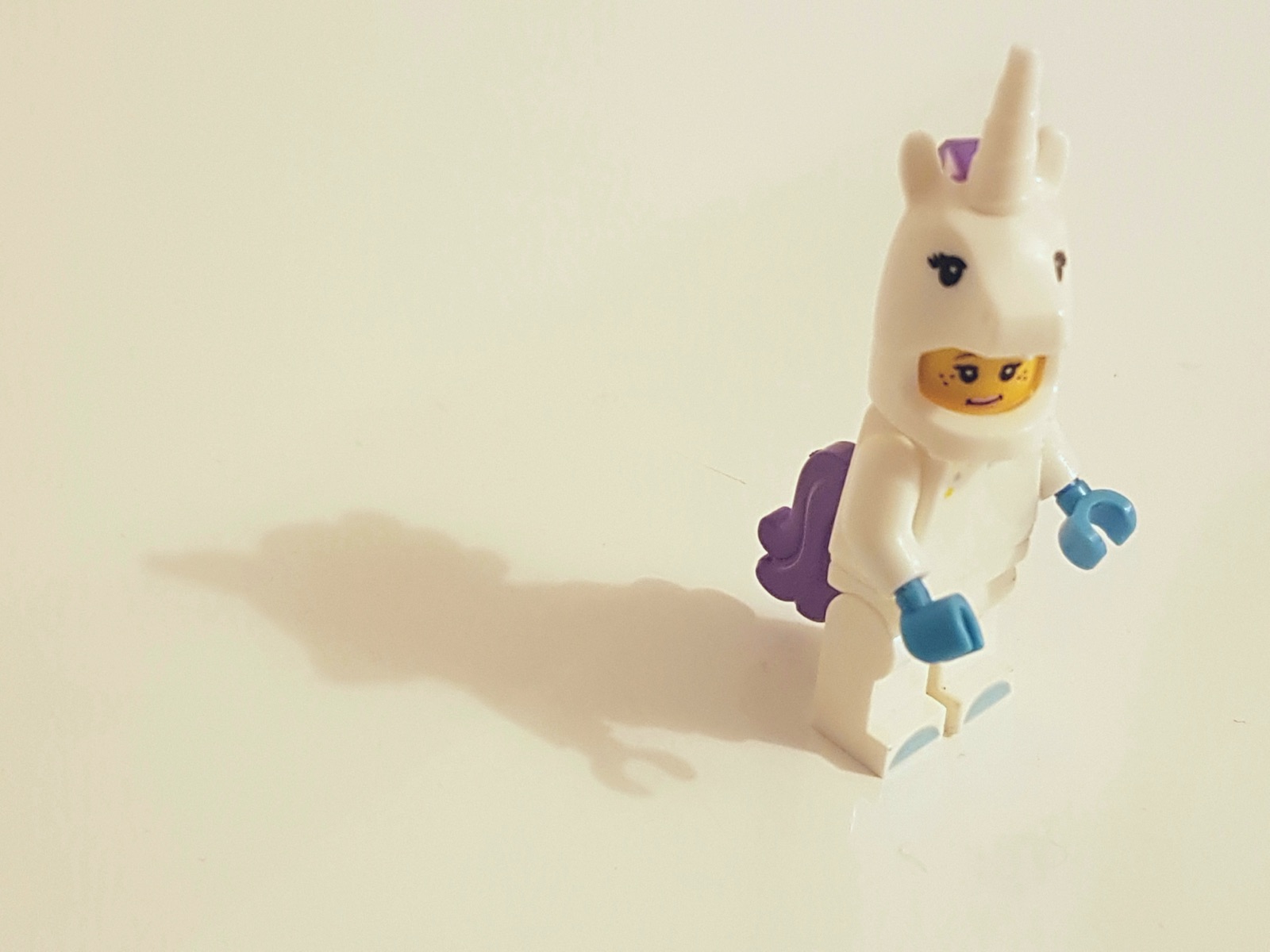 LEGO minifigure in white unicorn costume with purple mane and blue accessories