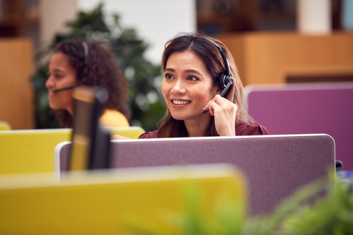 Smiling woman with headset working at computer in colorful office