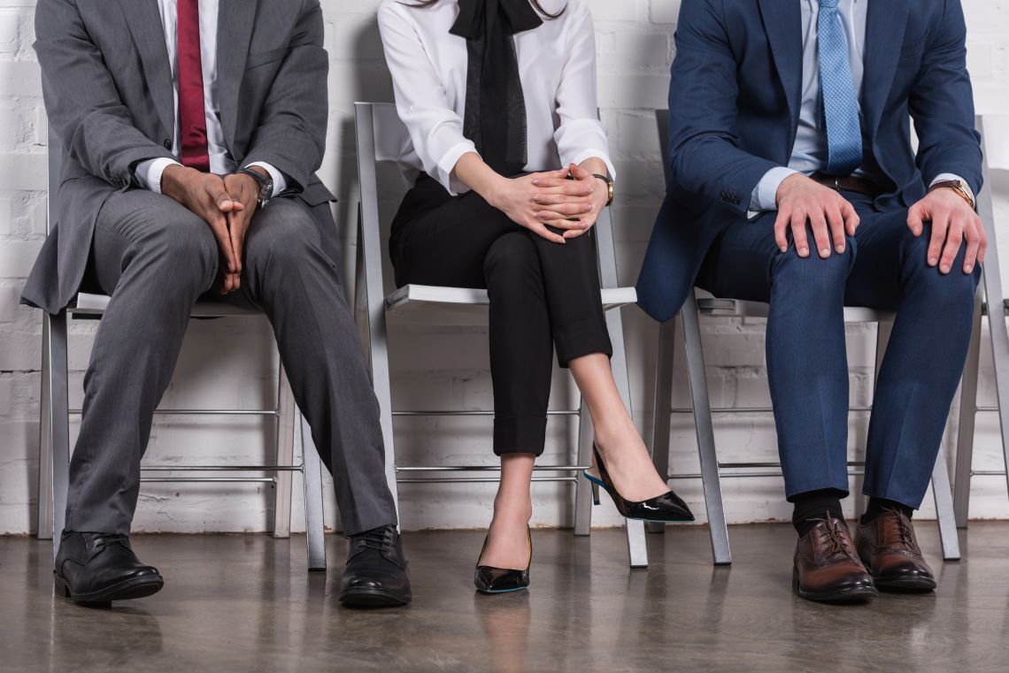 Three business professionals in suits sitting on chairs waiting